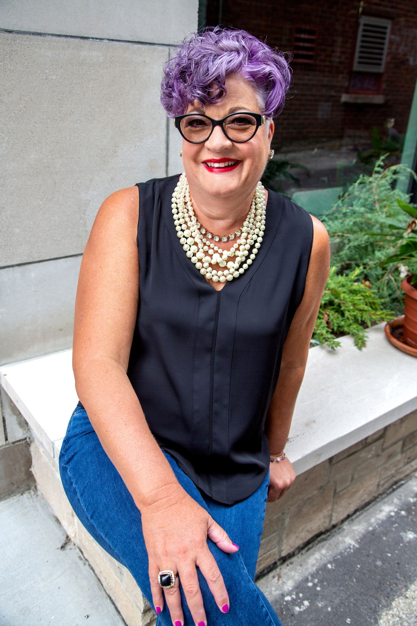 Brenda Florida seated outdoors in a black top and pearls, looking directly at the camera